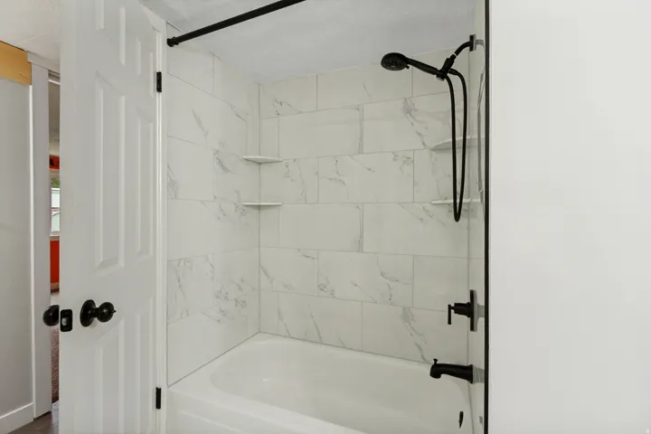 Bathtub with subway tile surround, corner shelving, and matte black fixtures including a shower head and faucet