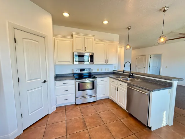 Kitchen featuring white shaker-style cabinetry, stainless steel appliances, dark countertops, and tile flooring