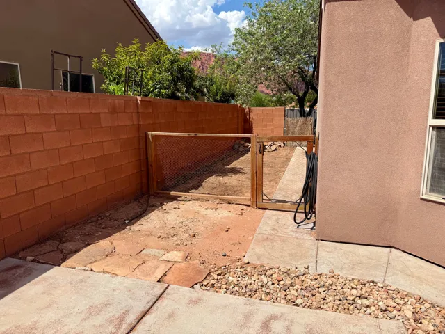 Partial concrete patio with a rock border, leading to a fenced enclosure