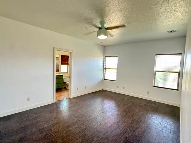 Spacious room with dark wood-finish flooring, white walls, two windows with blinds, and a ceiling fan with integrated lighting