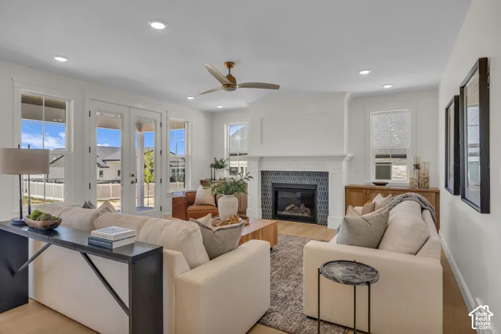 Living area featuring wood-finish flooring, a tiled fireplace with mantel, French doors, recessed lighting, and a ceiling fan