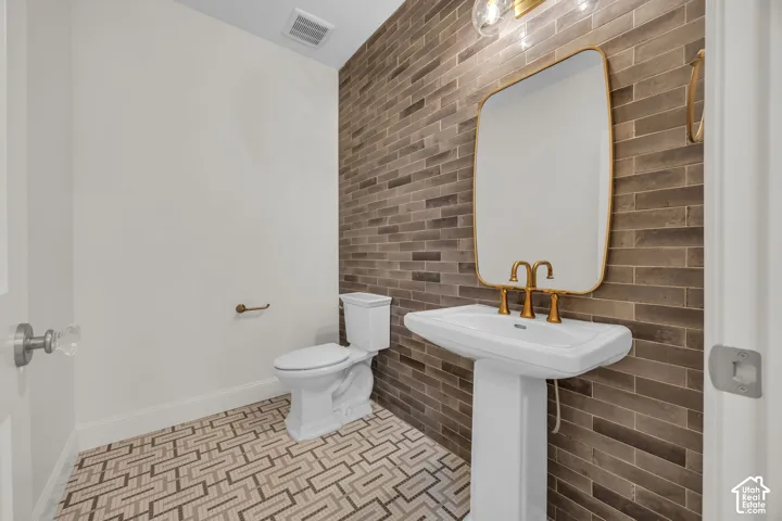 Pedestal sink with brass-finish fixtures, a rectangular mirror, and a wall of horizontal tile