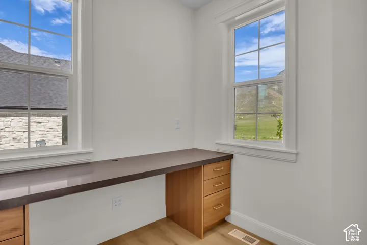 Built-in desk with a smooth countertop, light wood cabinetry, and multiple drawers