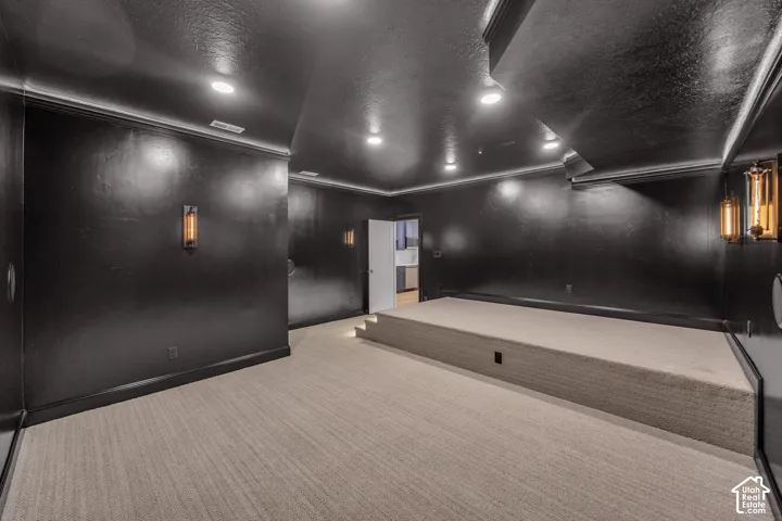 Carpeted entertainment room featuring a raised platform, recessed lighting, and decorative wall sconces