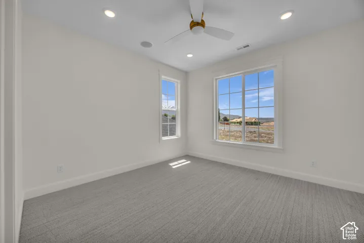 Recessed ceiling lighting, ceiling fan, two windows with white trim, and light gray patterned carpeting