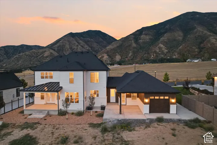 Modern farmhouse exterior with white siding, covered patio, attached garage, and mountain backdrop