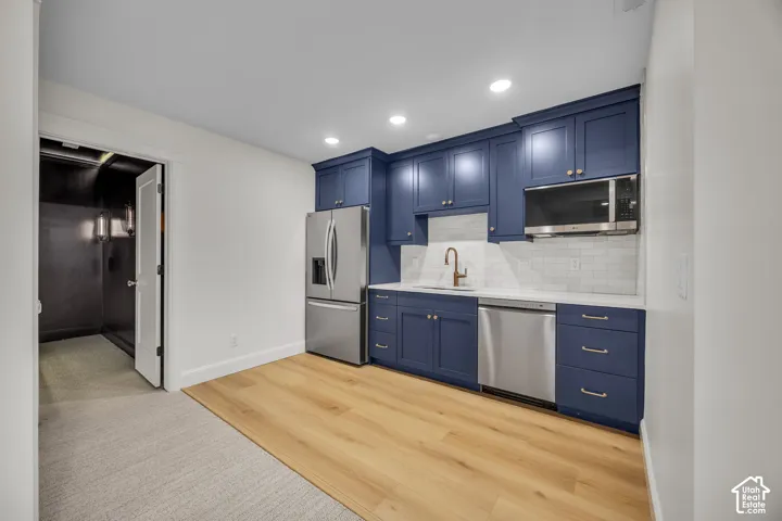 Kitchenette featuring navy cabinetry, white subway tile backsplash, stainless steel appliances, and wood-finish flooring