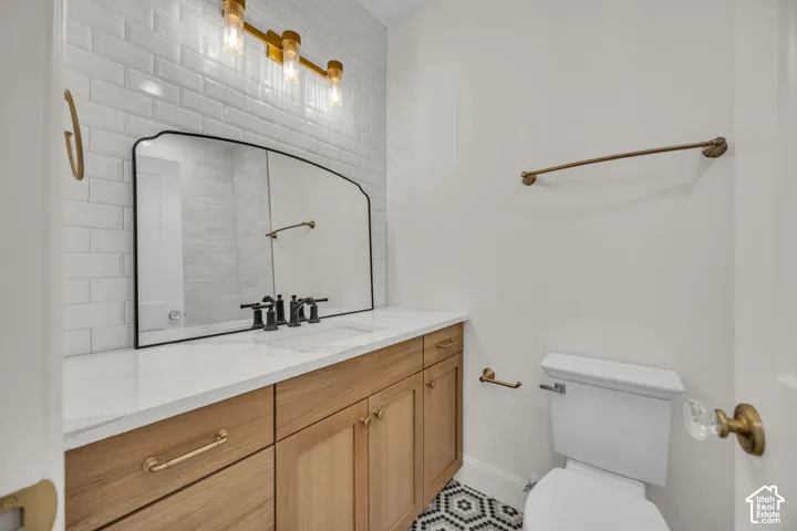 Wood-finish vanity with gold-tone hardware, white countertop, subway tile backsplash, and hexagonal floor tile