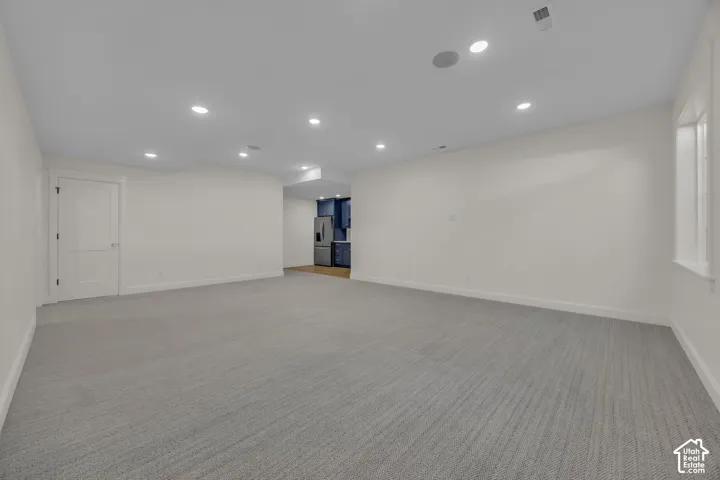 Spacious room featuring light gray patterned carpet, white walls, recessed ceiling lights, and a white interior door