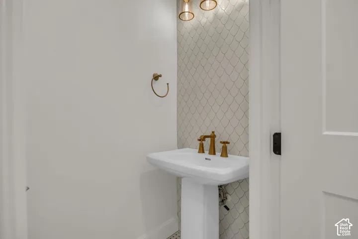 Pedestal sink with brass-finish faucet, scale-patterned accent wall, and brass-finish towel ring