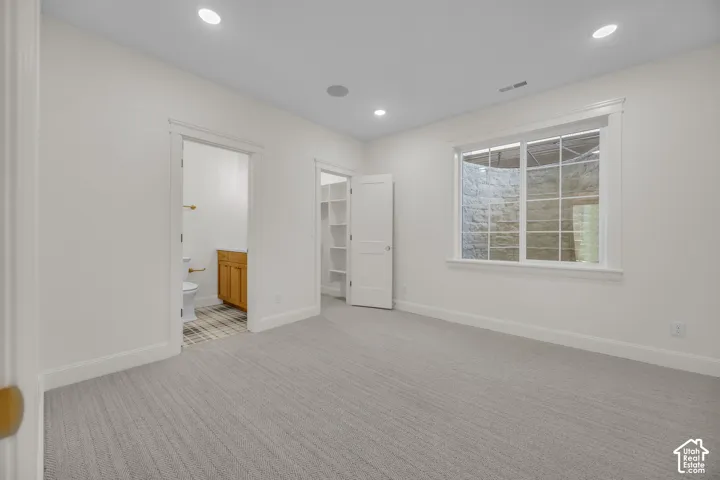 Neutral carpeting, recessed lighting, and a window with a stone window well