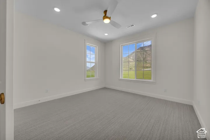 Neutral tone wall paint, textured carpeting, recessed lighting, ceiling fan, and two windows with white trim