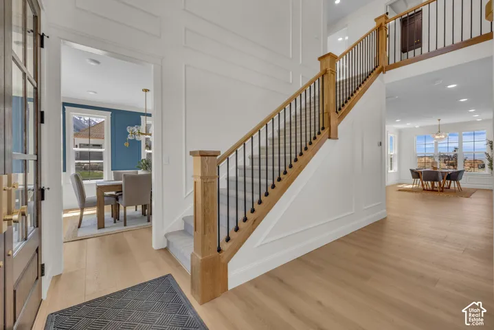 Wood-finish flooring throughout, grand staircase with wood banister and wrought iron spindles, wainscoting on walls, transom window above entryway, and recessed lighting
