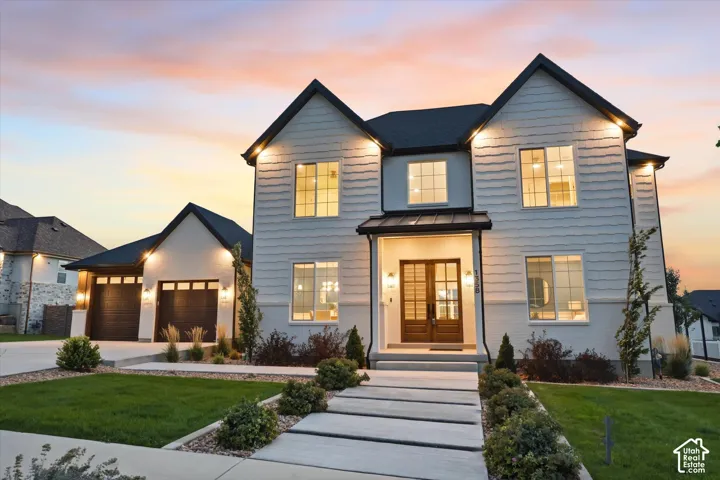 Modern exterior with light siding and dark trim, featuring a two-car garage, manicured landscaping, and a concrete paver walkway