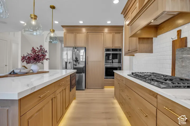Kitchen featuring natural wood cabinetry, white countertops, a gas range, built-in double ovens, and a large island with pendant lighting