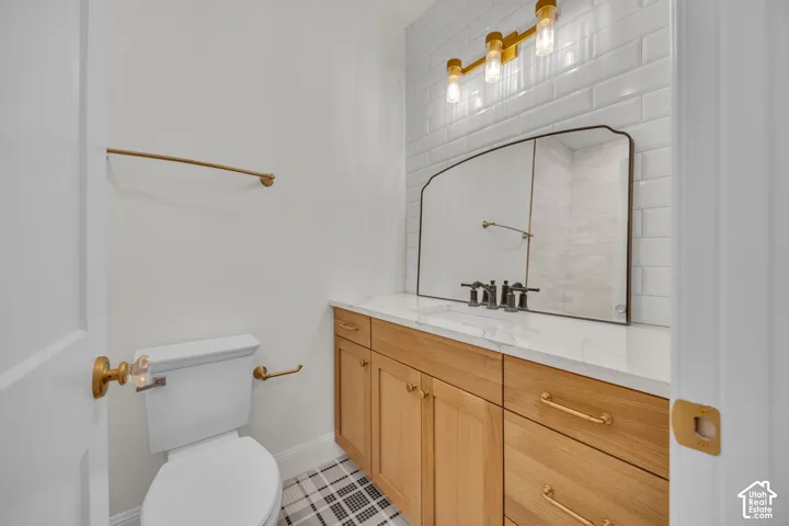Wood-finish vanity with a light-toned countertop, subway tile backsplash, and decorative wall-mounted light fixture