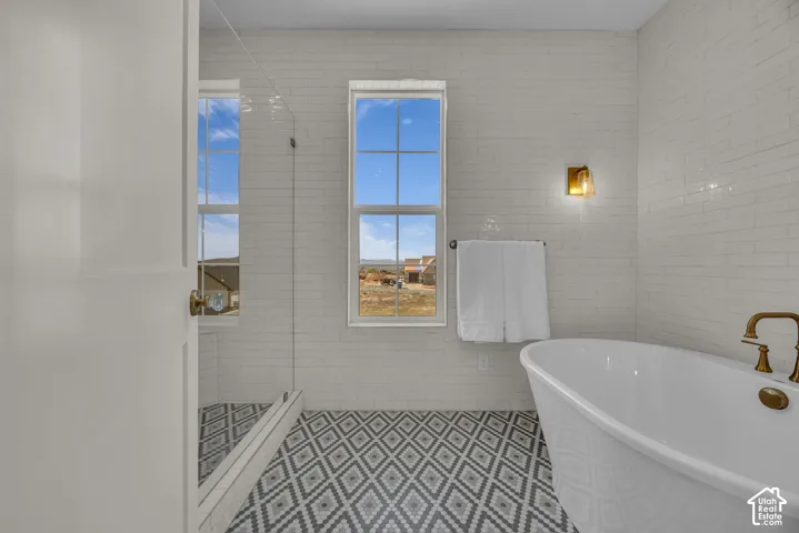 Freestanding soaking tub with brass fixtures, glass-enclosed shower, patterned floor tile, white subway tile walls, and dual pane windows
