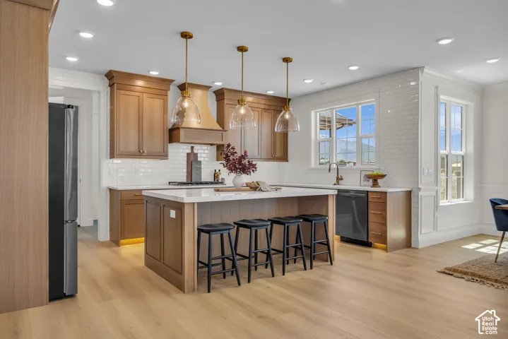 Kitchen featuring wood-finish cabinetry, a large center island with seating, pendant lighting, white subway tile backsplash, and light wood-finish flooring