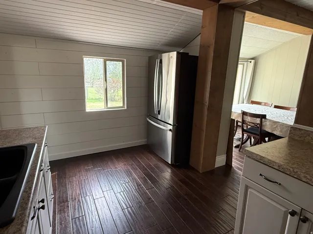 Wood-finish flooring, shiplap wall treatment, white cabinetry, and stainless steel refrigerator