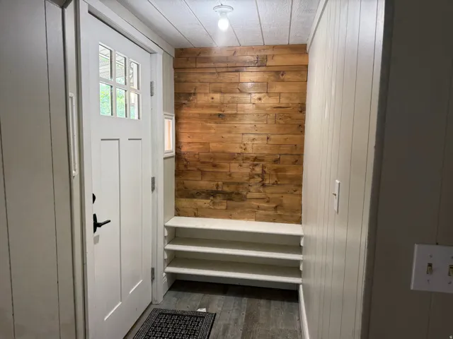 Craftsman-style entry door with glass panels, wood-finish accent wall, built-in shelving, paneling, and wood-finish flooring