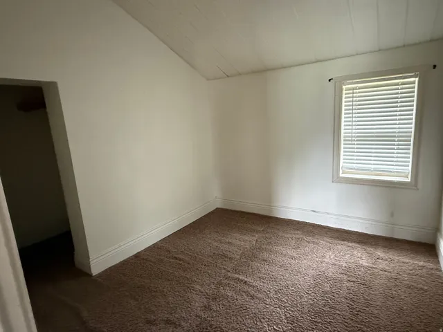 Carpeted room with a paneled ceiling, single window with blinds, and white trim