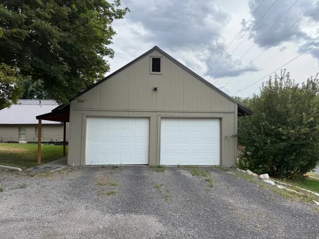 Detached structure featuring two paneled garage doors, vertical siding, and a gable roof with an attic vent