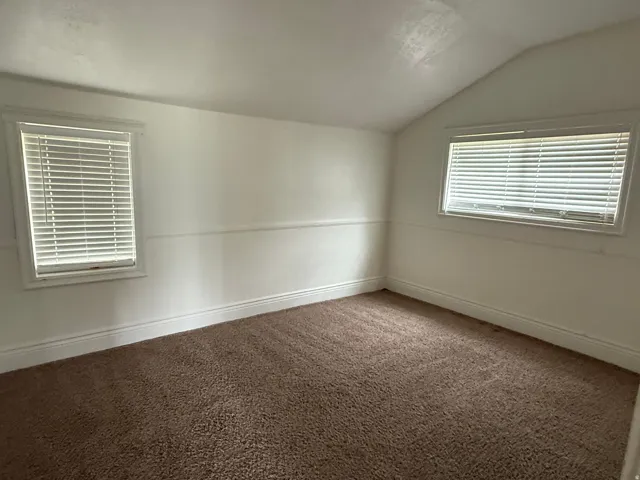 Carpeted room with white walls, two windows featuring horizontal blinds, and a sloped ceiling
