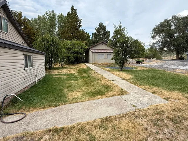 Siding exterior with a dark metal roof, concrete pathway, and mature trees
