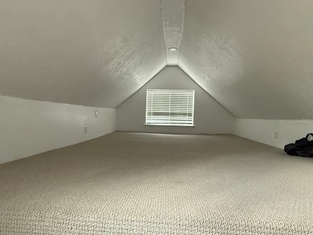 Carpeted loft space featuring an angled ceiling, recessed lighting, and a window with blinds