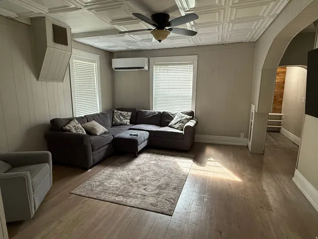 Textured ceiling panels with a ceiling fan, wood-finish flooring, and horizontal wall paneling