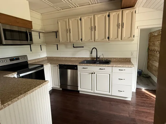 Kitchen featuring dark wood-finish flooring, white paneled walls, a tin-paneled ceiling, light-toned cabinetry, and stainless steel appliances