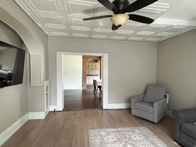 Textured ceiling panels, ceiling fan with light fixture, light wood-finish flooring, built-in display cabinet, and wide doorway