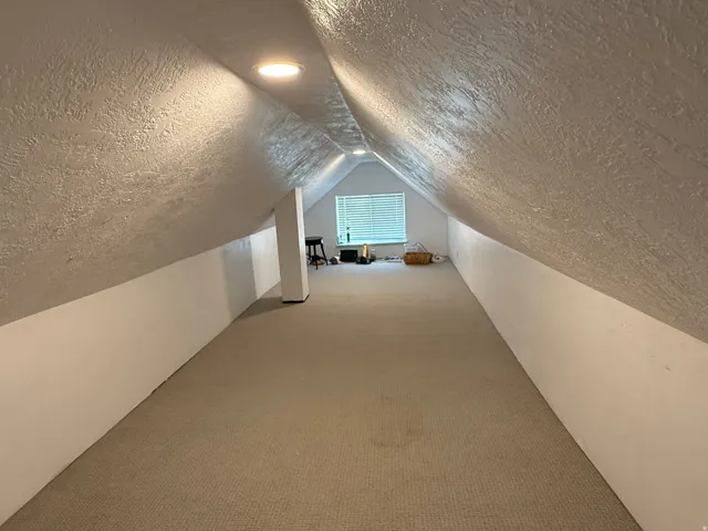 Carpeted attic space with sloped textured walls, recessed ceiling lighting, and a window with horizontal blinds