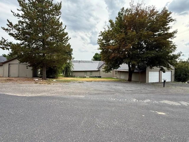 Expansive gravel driveway with mature trees, two detached garages, and a metal roof on the main structure