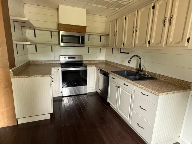 Kitchen featuring wood-finish flooring, white cabinetry, granite-style countertops, stainless steel appliances, and a black double-basin sink with a gooseneck faucet