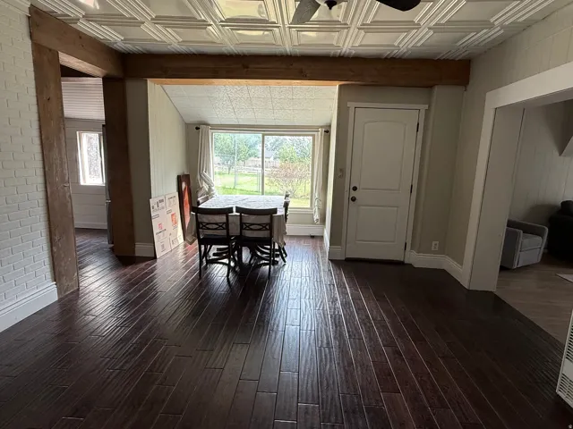 Dark wood-finish flooring, white pressed-tin ceiling, exposed wood beam, white brick accent wall, and a large picture window