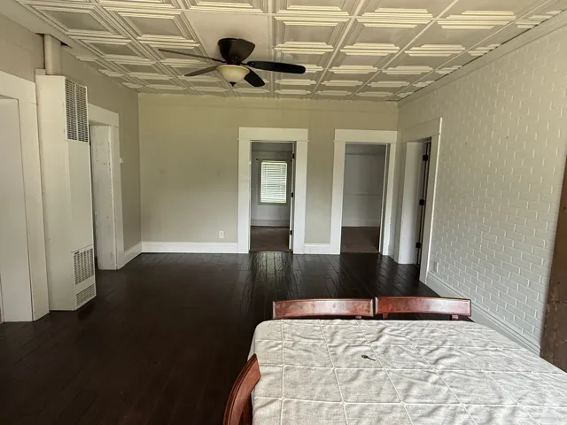 Dark wood-finish flooring, a textured white ceiling, and a ceiling fan with integrated lighting