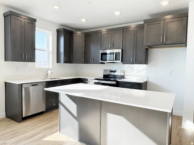Kitchen featuring dark wood-finish cabinetry, light countertops, a kitchen island, stainless steel appliances, and wood-finish flooring