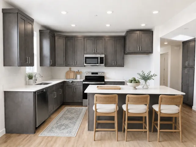 Modern kitchen featuring dark grey cabinetry, stainless steel appliances, white countertops, a central island with seating, and wood-finish flooring