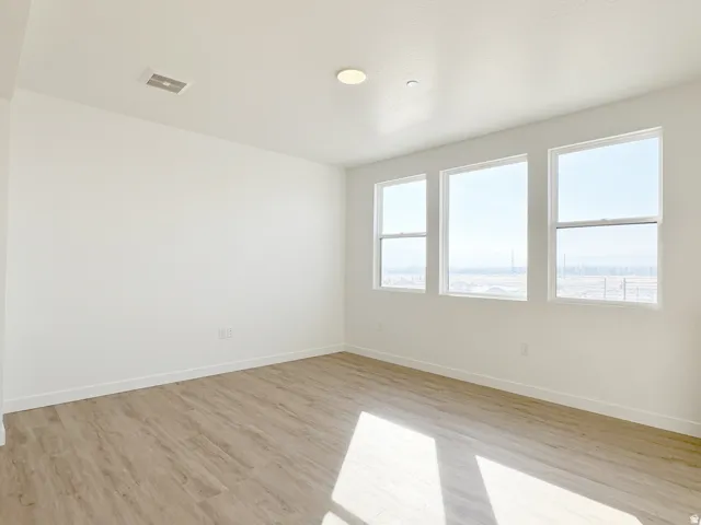 Bright interior space featuring three large windows, wood-finish flooring, recessed lighting, and a neutral color palette