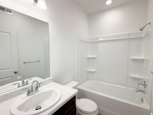 Vanity with an integrated sink and chrome faucet, full-width mirror, white bathtub with a shower kit, and recessed ceiling light