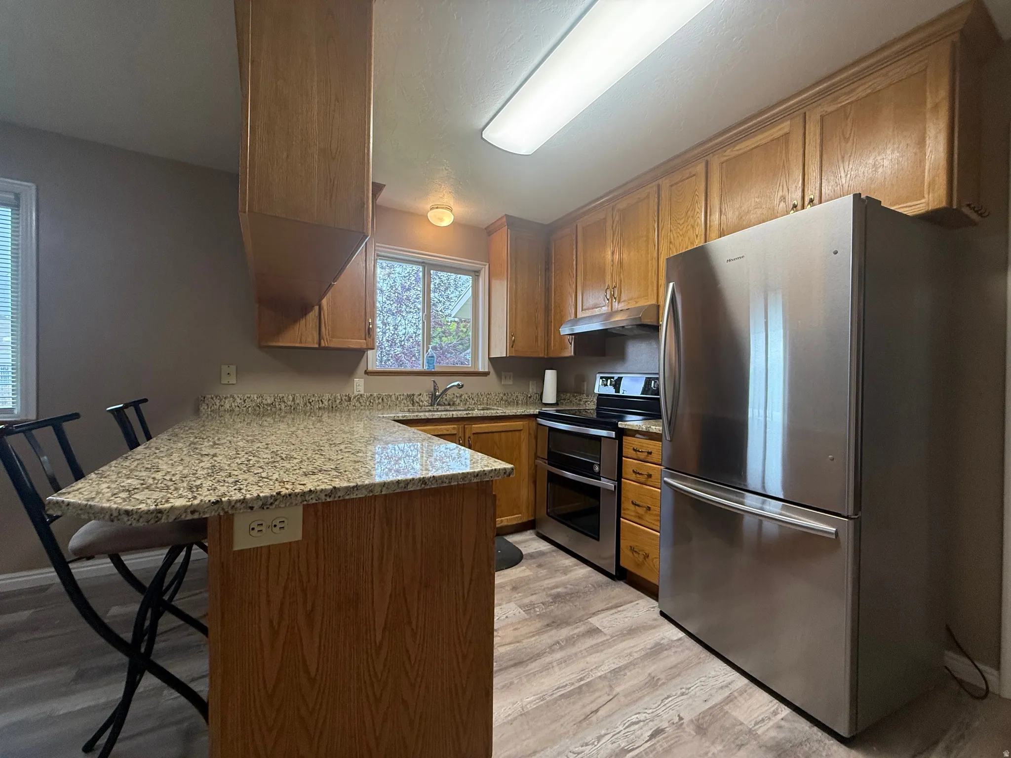 Kitchen with wood-finish cabinetry, granite-style countertops, stainless steel appliances, and wood-finish flooring