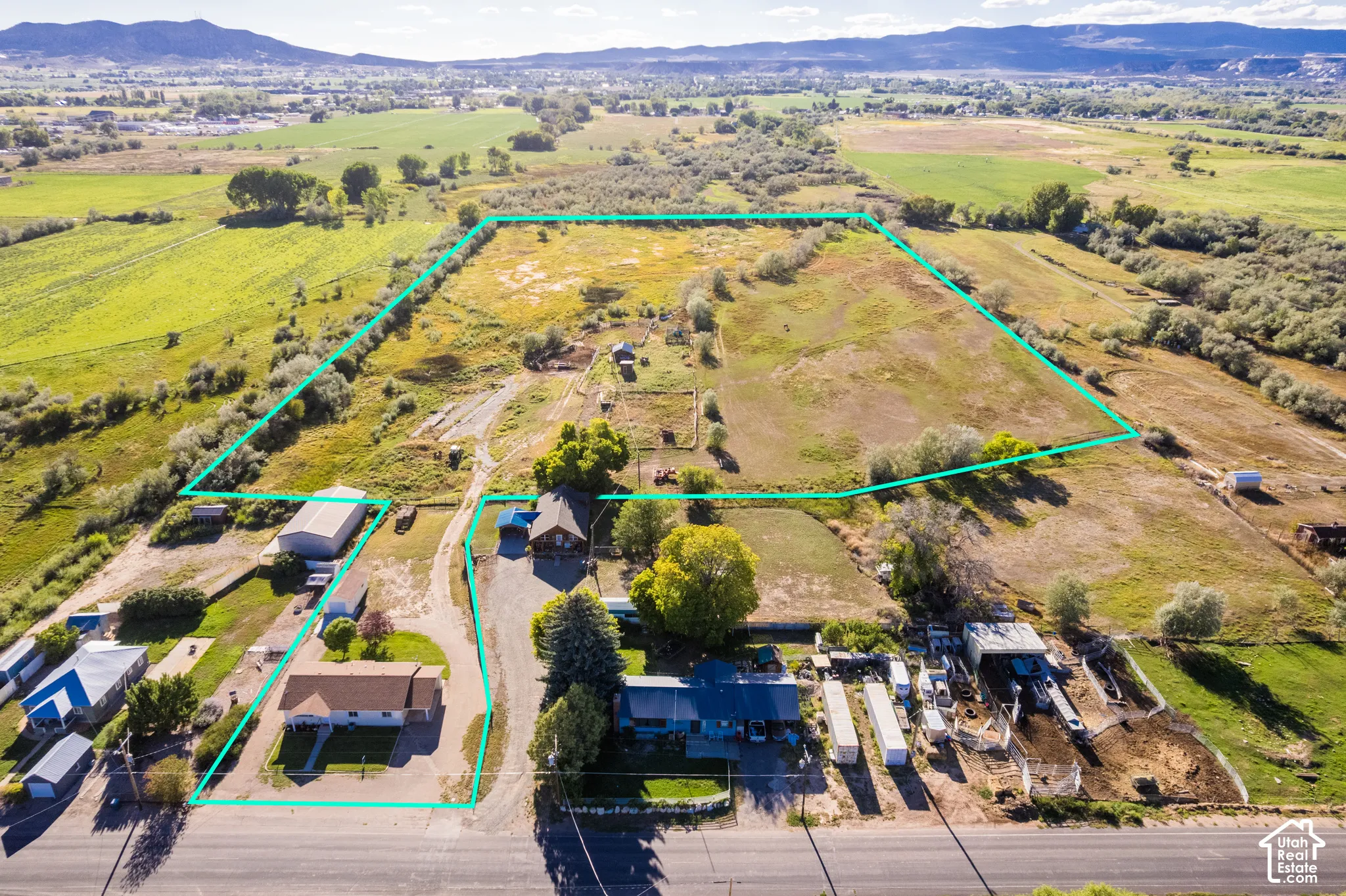 Expansive property featuring multiple structures, open land, paved road frontage, and a mountain backdrop