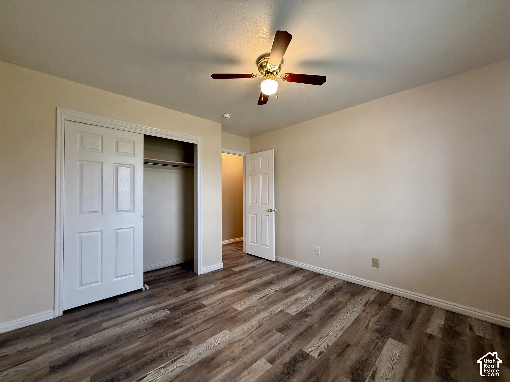Wood-finish flooring, ceiling fan with light fixture, neutral wall palette, bi-fold closet doors, and interior paneled door