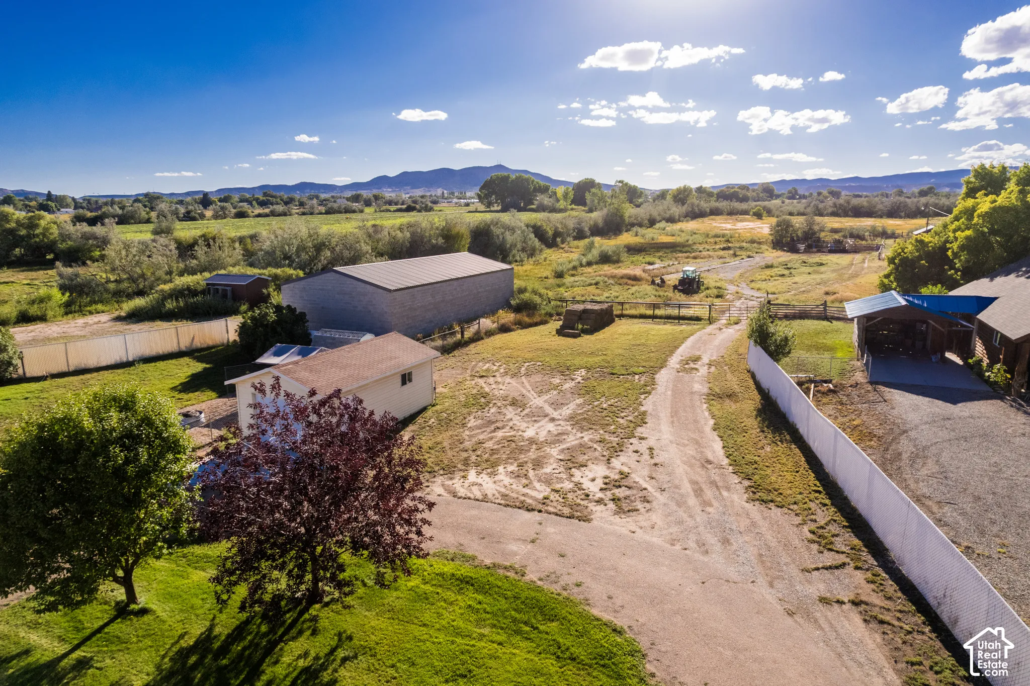 Expansive rural property featuring multiple structures, a gravel driveway, a large metal-roofed outbuilding, and a white privacy fence
