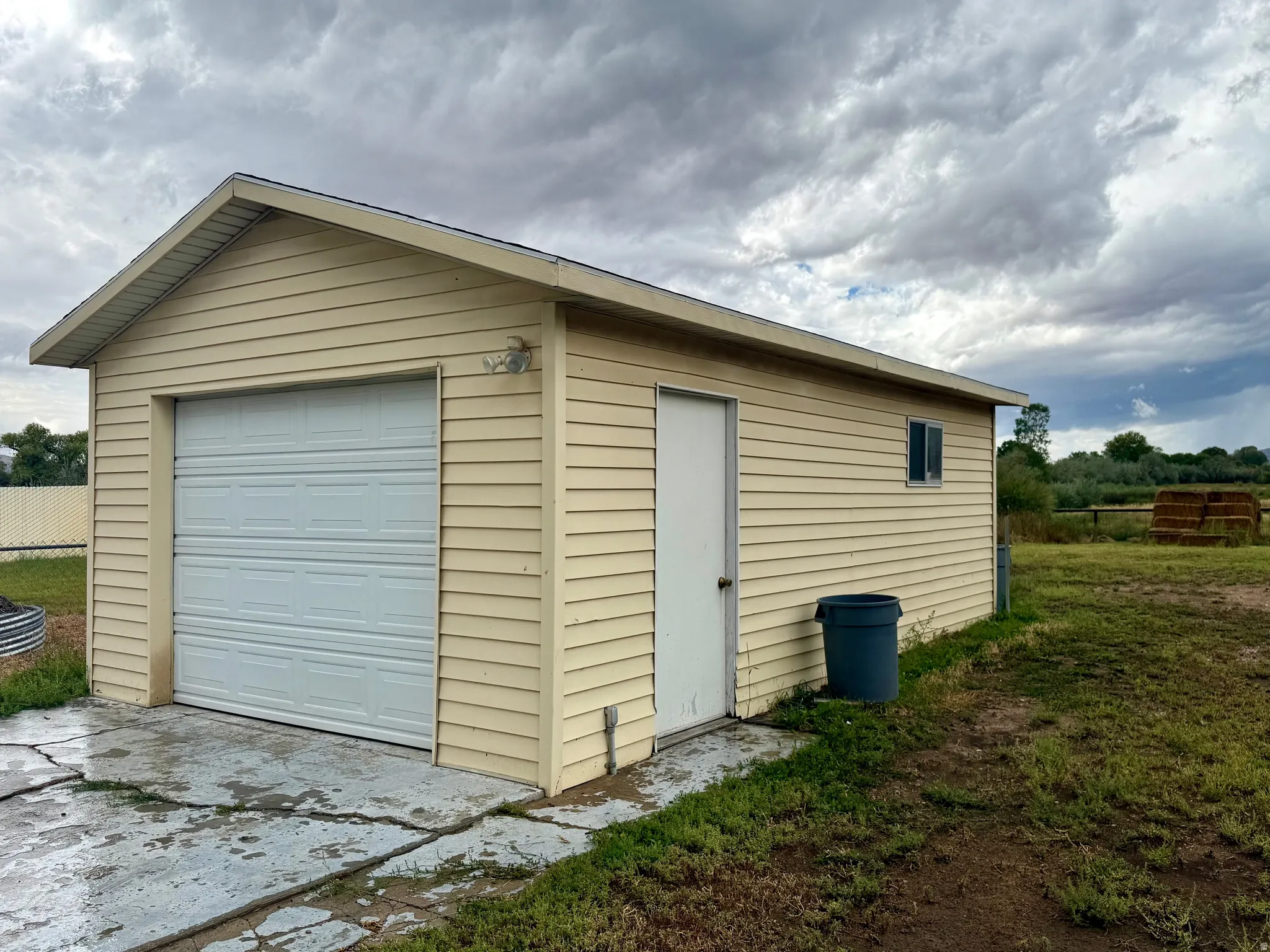 Detached outbuilding with light-colored siding, a single garage door, a side entry door, and a window