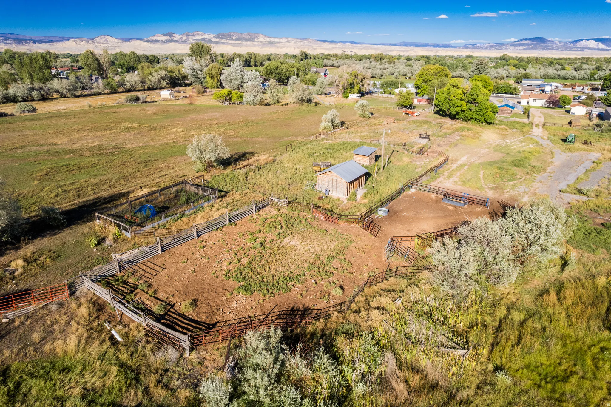 Multiple fenced areas, a detached outbuilding, expansive arid terrain, and distant natural scenery