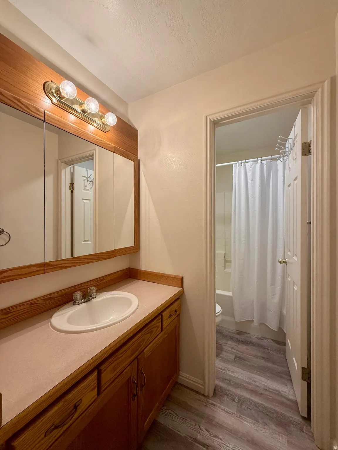 Bathroom featuring a wood-finish vanity with an integrated sink, laminate countertop, and a medicine cabinet with an overhead light fixture