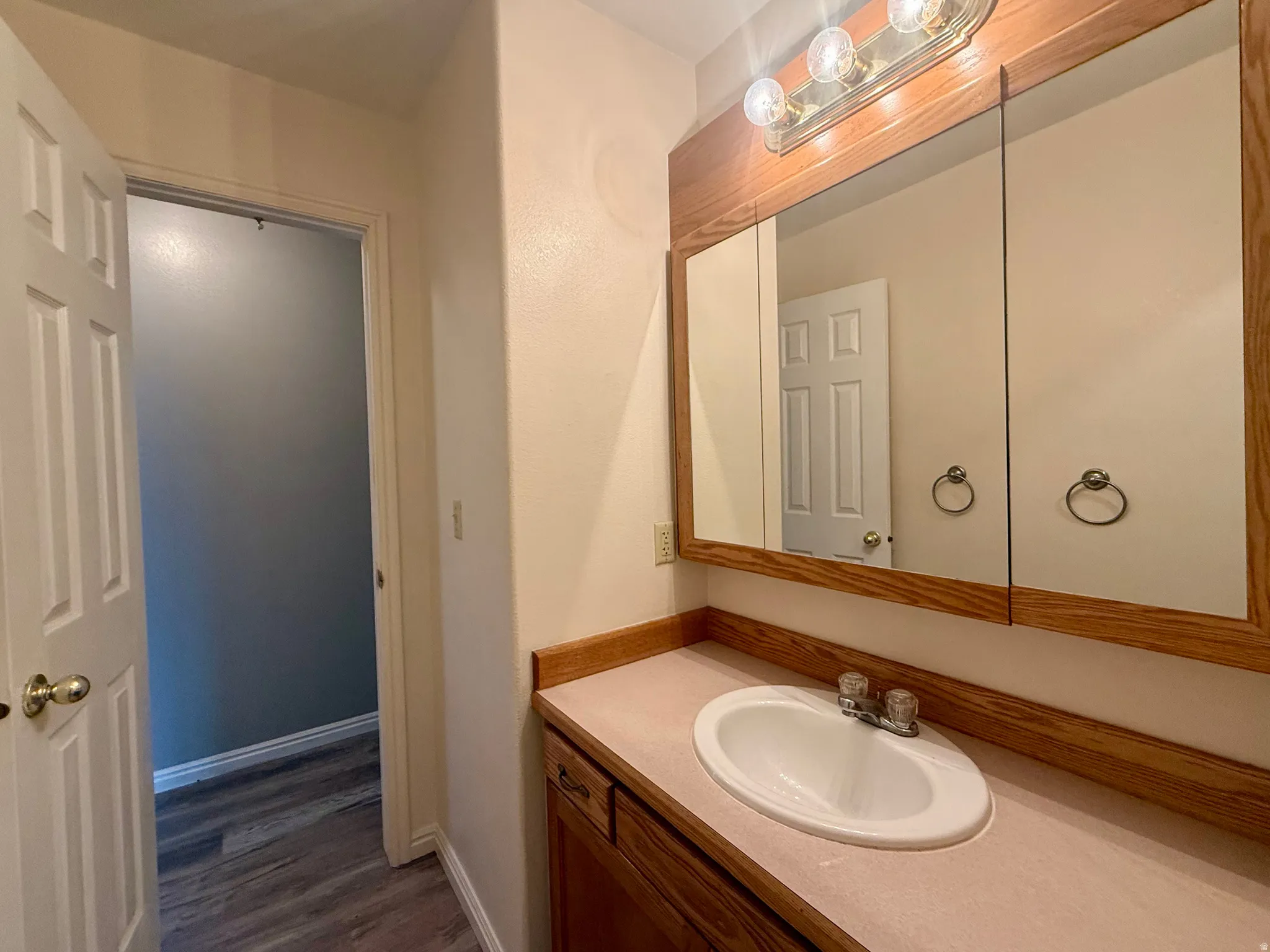 White oval sink with chrome faucet, wood-finish vanity with drawer, and a matching wood-finish medicine cabinet with integrated lighting