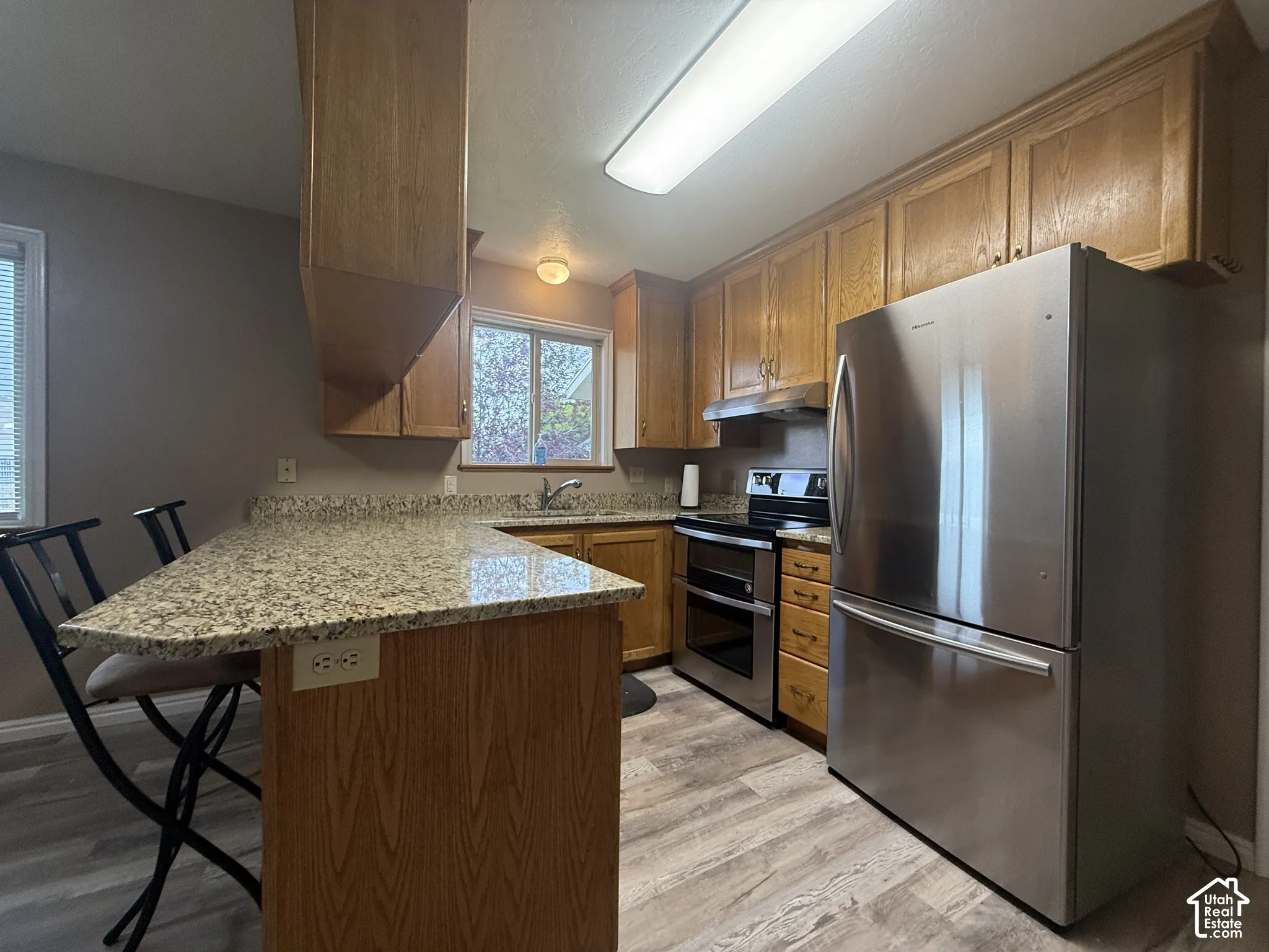 Kitchen with wood-finish cabinetry, granite-style countertops, stainless steel appliances, and wood-finish flooring